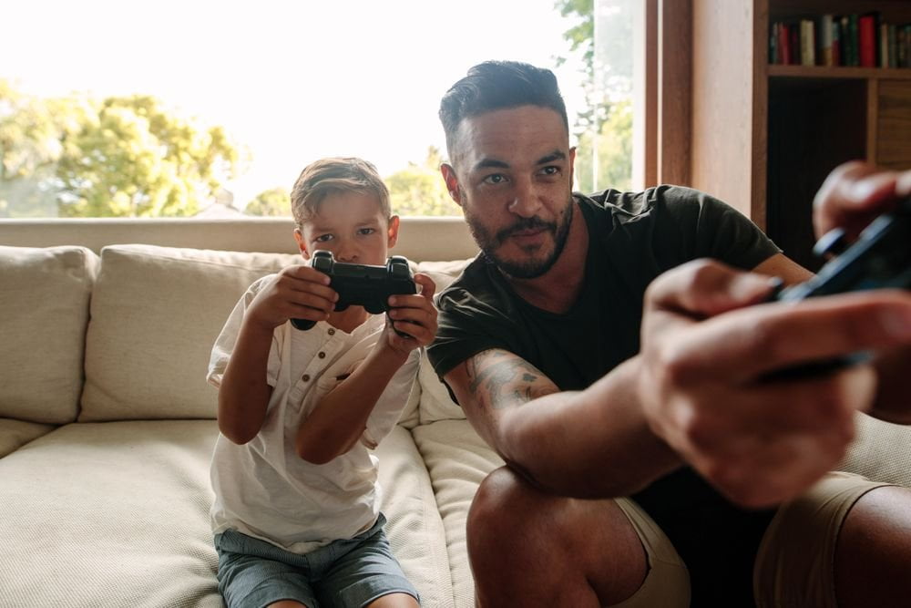 Father and young son, look intensely forward, holding video game controllers.