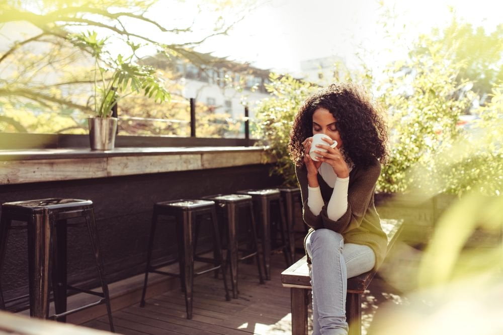 Women sits in a peaceful outdoor patio area, drinking a cup of coffee.