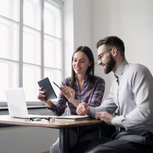 Two professionals sit at a desk reviewing data on a tablet